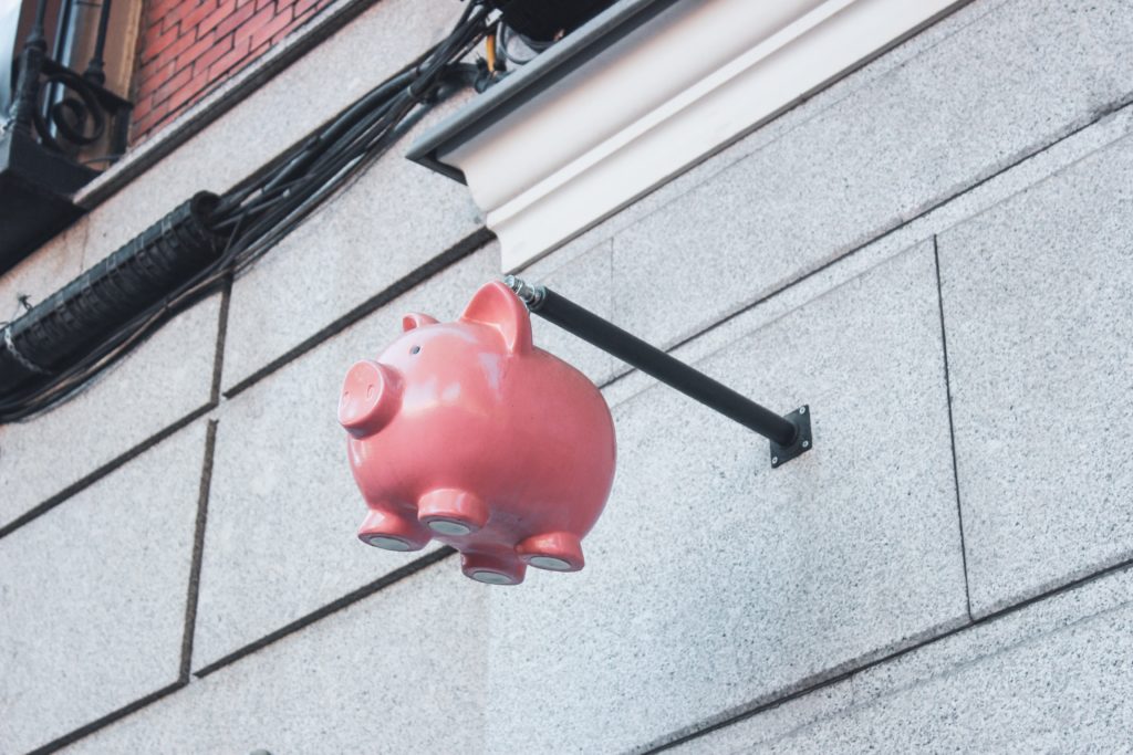 A pink piggy bank hangs from a post in a wall